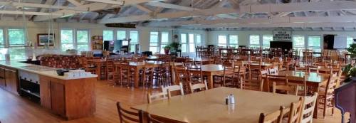 A spacious dining area with wooden tables and chairs, large windows, and a bright, airy atmosphere.