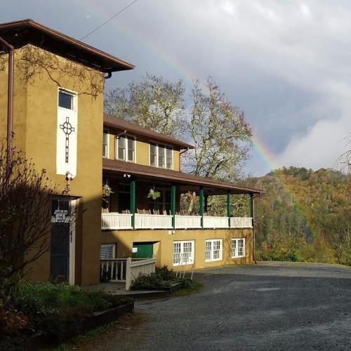 A rustic building with a porch, surrounded by trees, and a rainbow in the background after a rainstorm.
