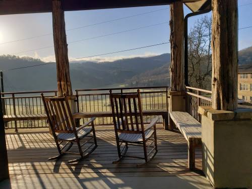 Two rocking chairs on a porch overlooking a scenic mountain view with soft morning light.