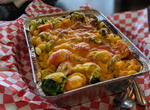 A metal tray filled with cheesy baked pasta and vegetables, surrounded by red and white checkered paper.