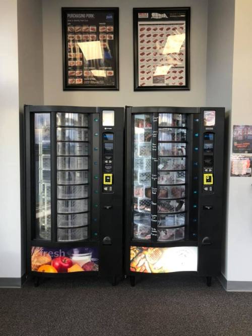 Two vending machines side by side, filled with various food items, in a well-lit indoor space.