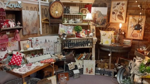A cozy shop display filled with rustic decor, artwork, and various home goods arranged on tables and shelves.