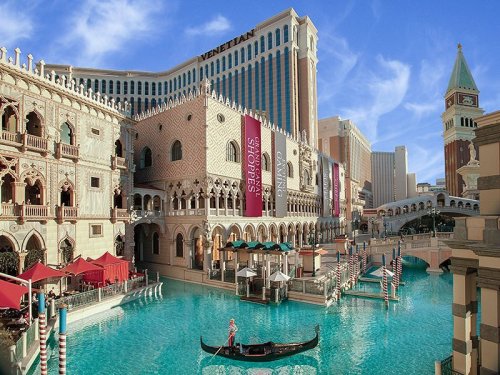 A scenic view of the Venetian Resort in Las Vegas, featuring a canal, gondola, and ornate architecture under a blue sky.