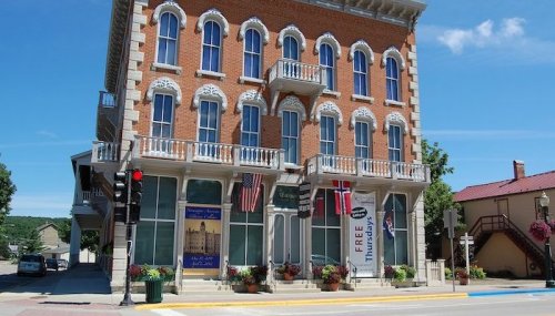 Historic brick building with balconies, flags, and banners, set against a clear blue sky in a small town.