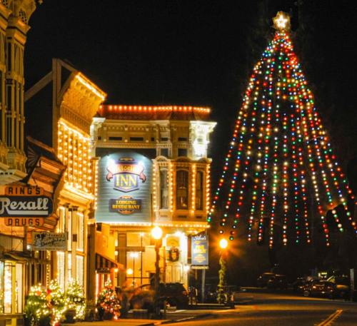 A festive street scene at night, featuring a large decorated Christmas tree and illuminated buildings.