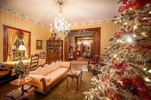 Cozy living room decorated for the holidays, featuring a Christmas tree, vintage furniture, and warm lighting.