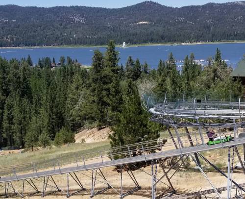 A scenic view of a mountain landscape with a lake, featuring a winding roller coaster track and a green ride.