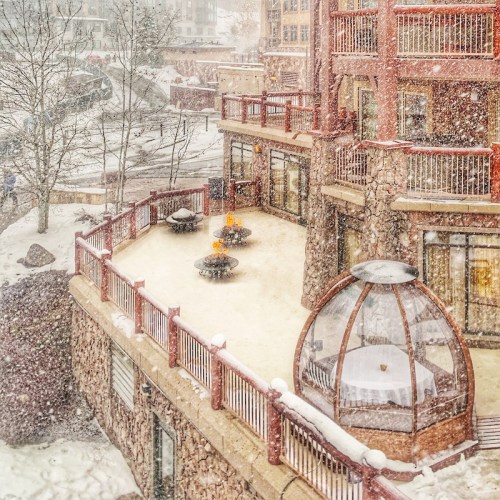 A snowy scene featuring a cozy building with a stone exterior and a circular glass structure on a winter day.