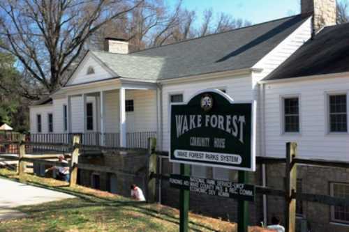 A white community house with a sign reading "Wake Forest Community House" and a grassy area in front.