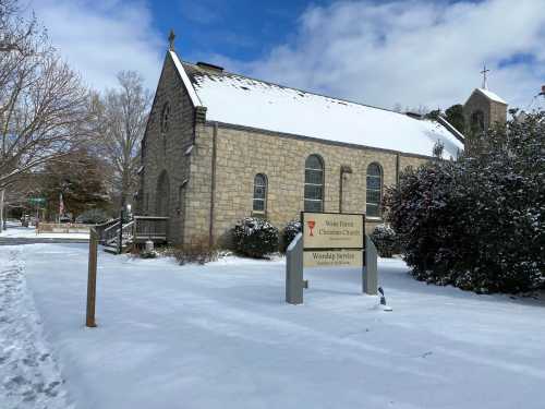 A stone church covered in snow, with a sign for Wake Forest Christian Church and a clear blue sky above.