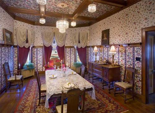 A vintage dining room with floral wallpaper, a large table set for dinner, and elegant chandeliers.