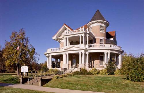 A large, elegant Victorian-style house with a turret, surrounded by greenery and a clear blue sky.