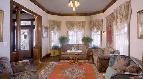 Cozy living room with patterned furniture, a round table, and large windows adorned with elegant drapes.