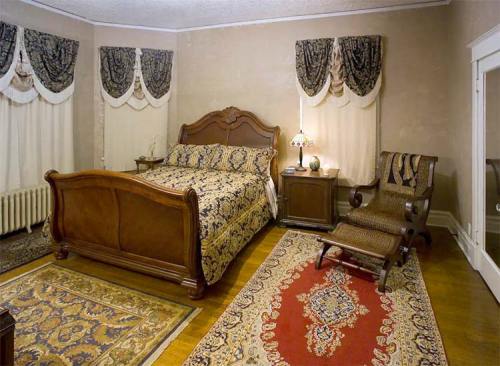 Cozy bedroom featuring a wooden bed, patterned bedding, a chair, and elegant curtains, with a decorative rug on the floor.