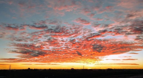 A vibrant sunset with orange and pink clouds against a blue sky, silhouetting a distant horizon.