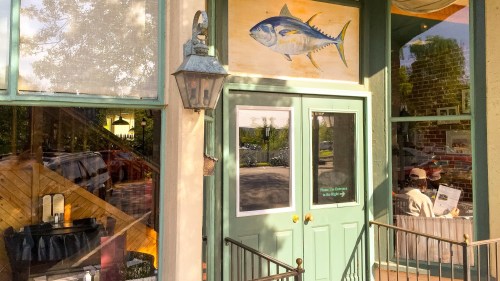 A restaurant entrance with a fish painting above the door and a person sitting inside looking at a menu.