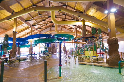 Indoor water park featuring colorful slides, water features, and seating areas under a spacious wooden ceiling.