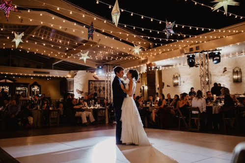 A couple dances together under string lights and stars at a festive evening reception, surrounded by guests.