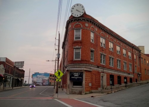 Historic red brick building with a large clock on top, located at a street intersection during twilight.