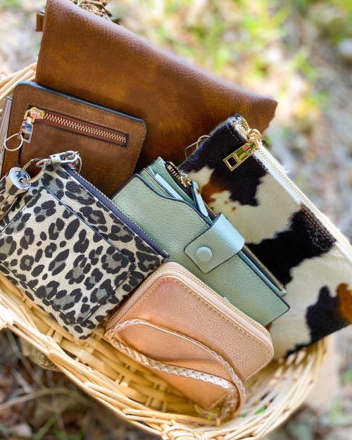 A variety of stylish wallets and pouches in a woven basket, featuring different textures and patterns.