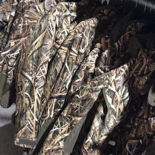A close-up of camouflage clothing hanging on a rack, featuring a pattern of grass and foliage.
