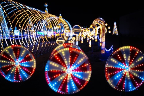 Colorful holiday lights create a festive display, featuring large candy cane and lollipop decorations against a dark background.