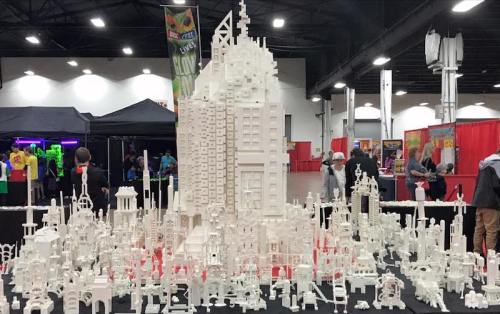 A large, intricate white building model surrounded by smaller structures, displayed at an event in a convention center.