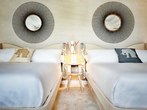 A stylish hotel room with two beds, decorative mirrors, and elephant-themed pillows on each bed.