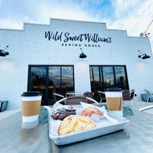 A table with baked goods and coffee cups outside Wild Sweet William's Baking House, featuring a bright sky and modern decor.