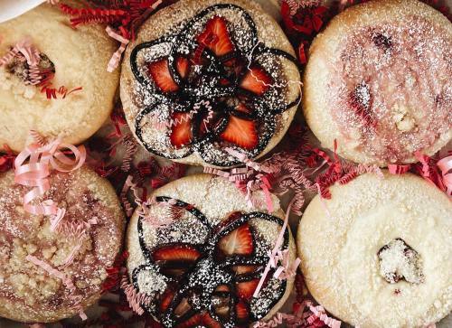 A box of decorated donuts with various toppings, including strawberries and chocolate, surrounded by colorful paper shreds.