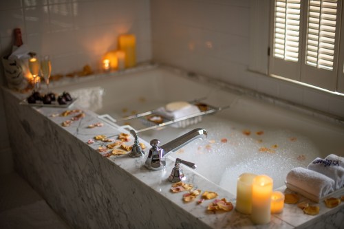 A luxurious bathtub filled with bubbles, surrounded by rose petals, candles, and champagne glasses.