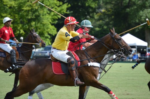 Two polo players in colorful uniforms riding horses, competing in a match on a grassy field.