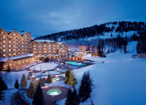 A luxurious hotel surrounded by snow-covered trees, featuring outdoor pools and a serene winter landscape at dusk.