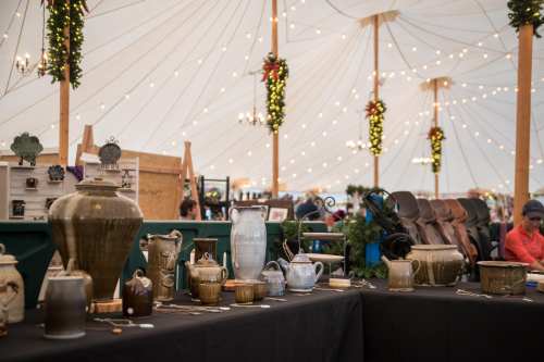 A display of various decorative pottery and vases under a festive tent with string lights and holiday decorations.
