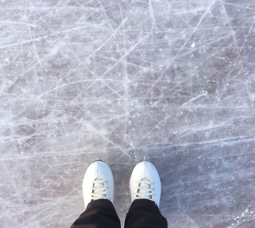 A pair of white ice skates on a textured ice surface with visible scratches and lines.