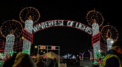 A festive archway reading "Winterfest of Lights," adorned with colorful lights and candles, set against a night sky.