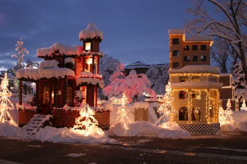 Two beautifully decorated buildings covered in snow, illuminated with colorful lights, surrounded by snowy trees.