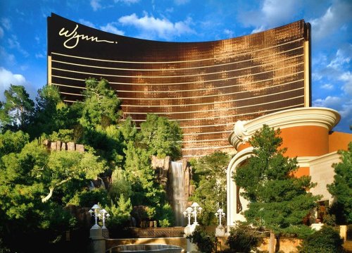 Wynn Las Vegas hotel with lush greenery and a waterfall in the foreground against a blue sky.