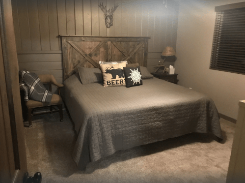 Cozy bedroom with a wooden bed, decorative pillows, and a chair, featuring warm tones and rustic decor.