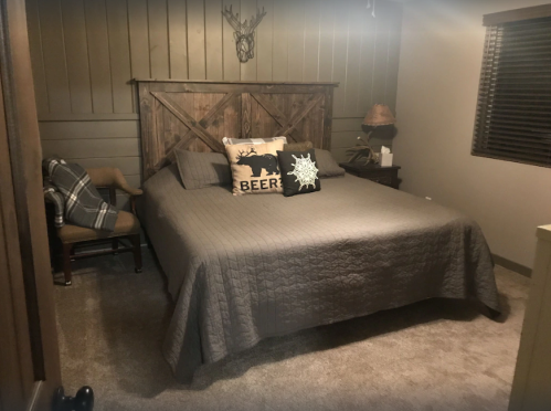 Cozy bedroom with a wooden bed, decorative pillows, and a chair, featuring warm tones and rustic decor.