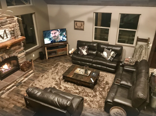 Cozy living room with leather sofas, a stone fireplace, and a TV displaying a scene, illuminated by warm lighting.