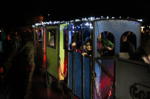 A colorful train with lights rides through a festive night, filled with people enjoying the atmosphere.