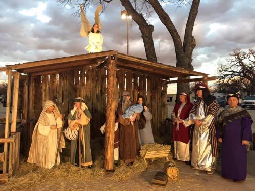 A nativity scene with figures depicting Mary, Joseph, and angels, set in a rustic stable under a cloudy sky.