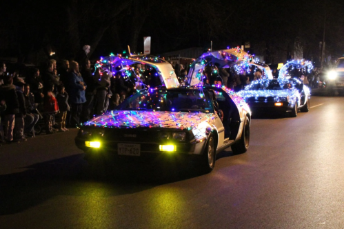 Two decorated cars with colorful lights drive past a crowd at night, creating a festive atmosphere.