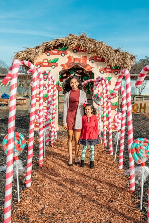 A woman and a girl stand together under a festive archway decorated with candy canes and holiday decorations.