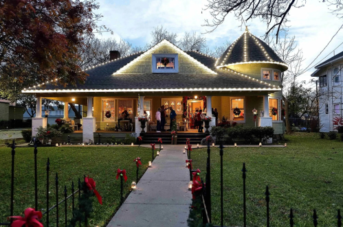 A beautifully decorated house with holiday lights, a festive walkway, and people gathered on the porch.