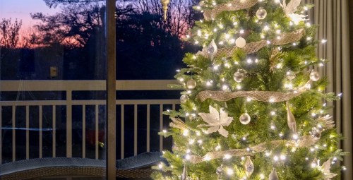 A beautifully decorated Christmas tree with lights and ornaments, set against a sunset view through a window.