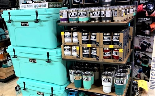 Display of YETI products, including coolers and tumblers, organized on shelves in a retail setting.