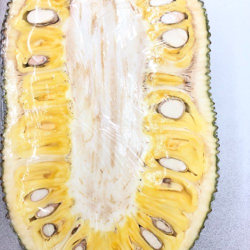 A halved jackfruit showing its yellow flesh and large seeds, with a textured green rind around the edges.
