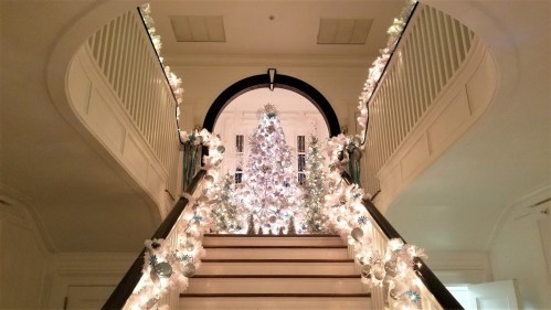 A beautifully decorated staircase with a white Christmas tree and twinkling lights, creating a festive atmosphere.